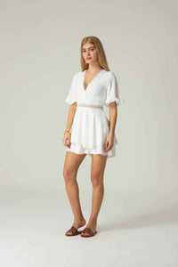 Woman wearing a white dress with lace details on a plain background.