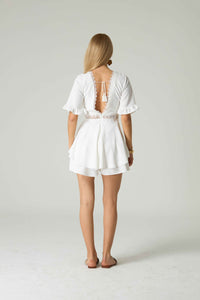 Woman wearing a white romper with lace details on a plain background.