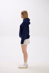 Side view of model in a navy blue hoodie paired with a light grey mini skirt, white socks, and sneakers.