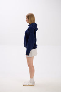 Side view of model in a navy blue hoodie paired with a light grey mini skirt, white socks, and sneakers.