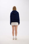 Back view of model in a navy blue hoodie paired with a light grey mini skirt, white socks, and sneakers.