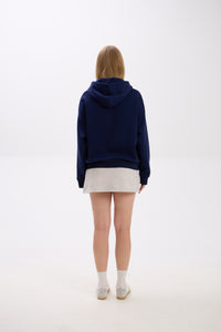 Back view of model in a navy blue hoodie paired with a light grey mini skirt, white socks, and sneakers.
