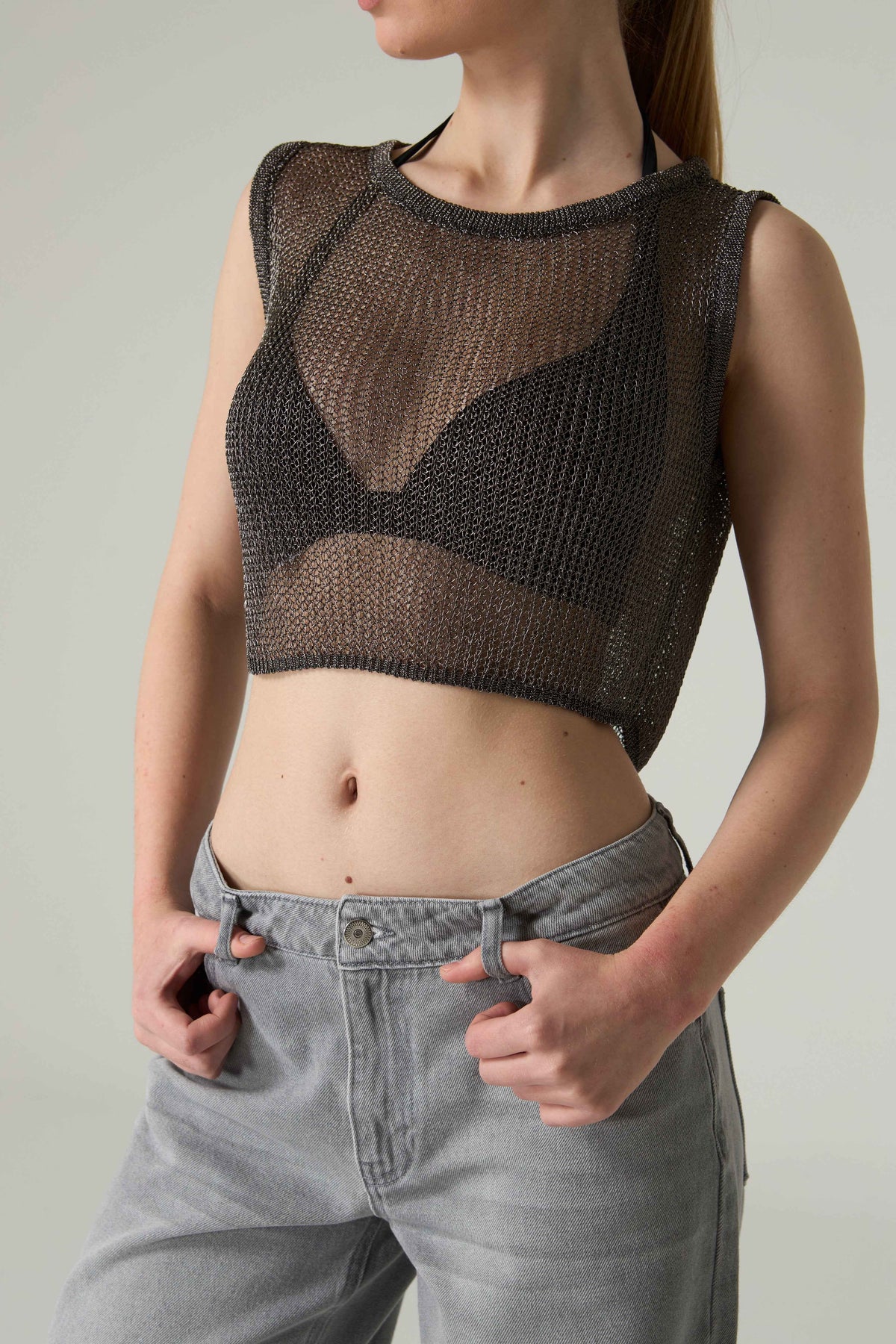 Person wearing a brown knit crop top and gray pants against a neutral background.