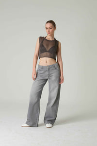 Woman wearing a sheer black top and gray pants on a plain background.