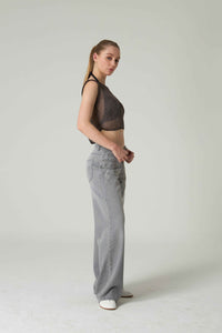 Woman wearing a black sheer top and gray pants on a white background.