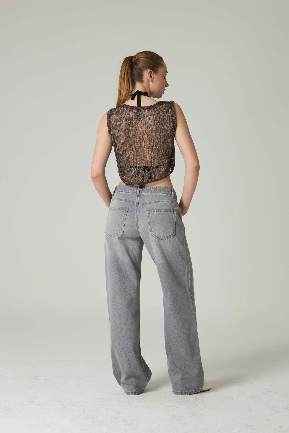 Person wearing a sheer top and gray pants on a plain background.