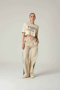 Person wearing a beige crop top with 'Paris Parade'  embroidery and pants on a light gray background.