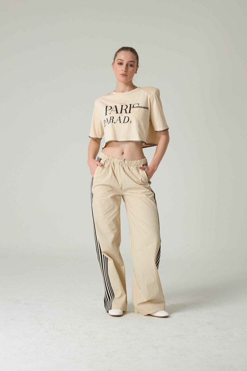 Person wearing a beige t-shirt and pants with stripes on a white background.