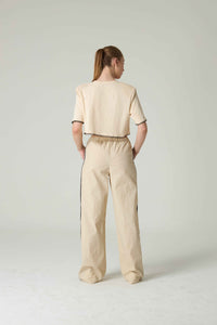 Person wearing a beige outfit with black trim on a plain background.