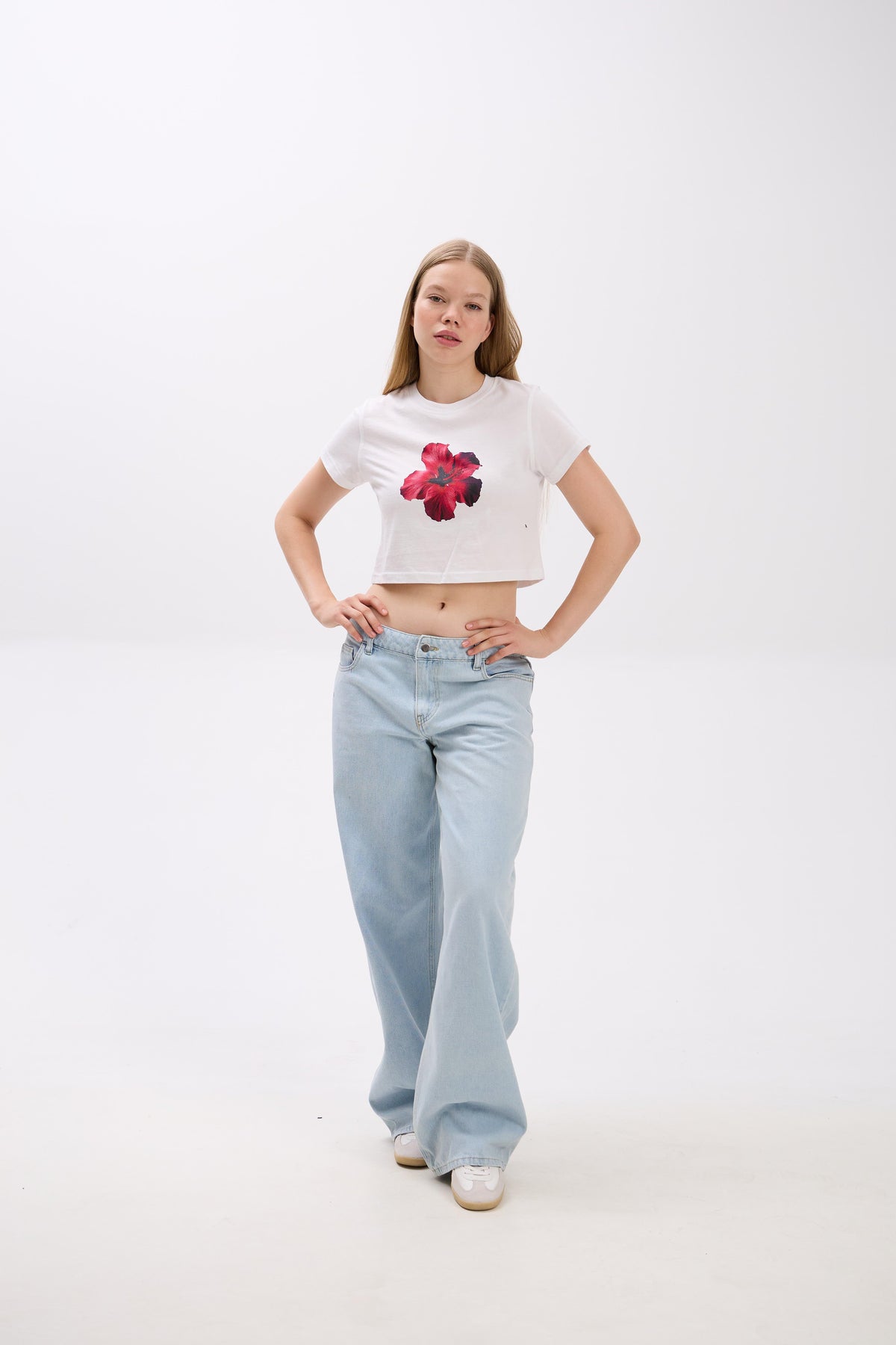 Person wearing a white crop top with a red floral design and light blue jeans on a white background.