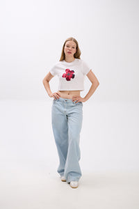 Person wearing a white crop top with a red floral design and light blue jeans on a white background.