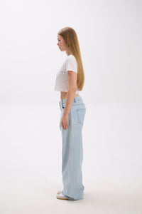 Woman wearing light blue jeans and a white top on a white background.