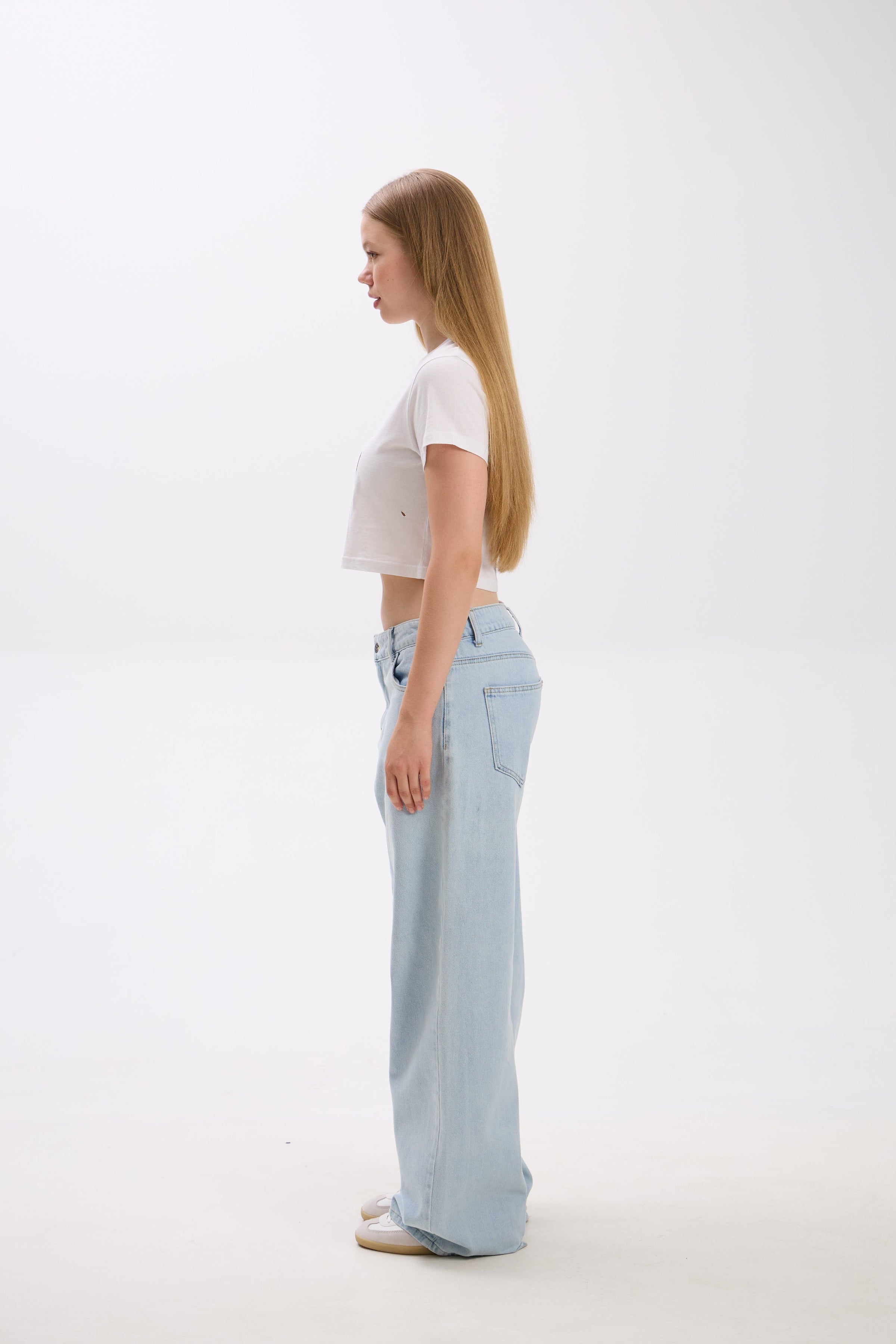 Woman wearing light blue jeans and a white top on a white background.
