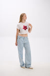 Woman wearing a white t-shirt with a red floral design and light blue jeans on a white background.