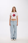 Person wearing a white crop top with a red flower design and light blue jeans on a white background.