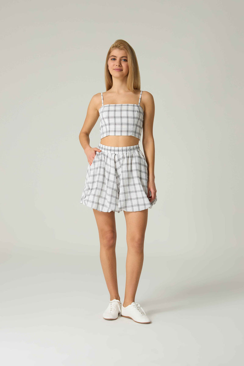 Woman wearing a checkered outfit with a top and shorts on a plain background.