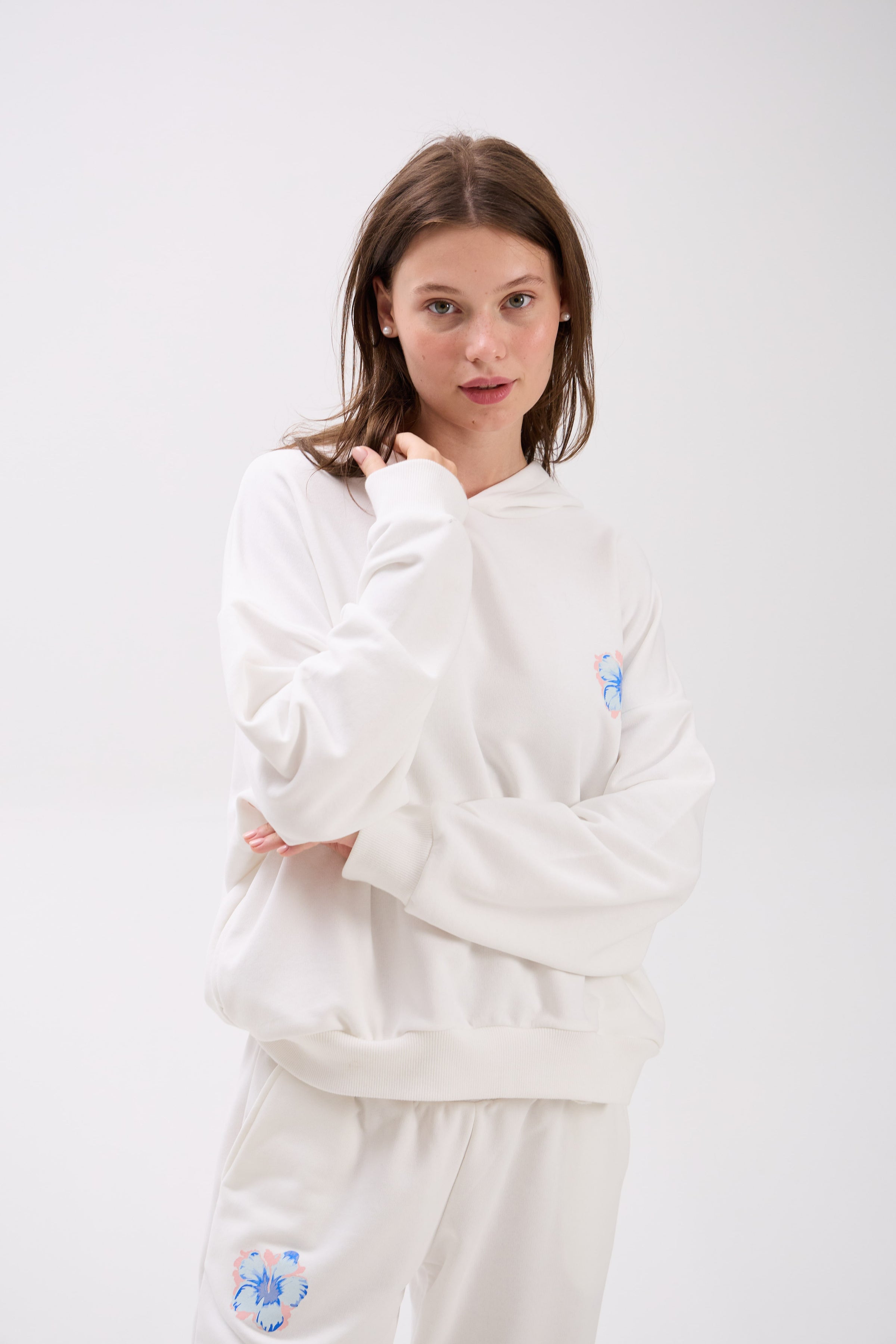 Woman wearing a white hoodie with a small logo on a light gray background.