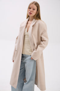 Woman wearing a beige coat over a white top and light blue jeans on a white background