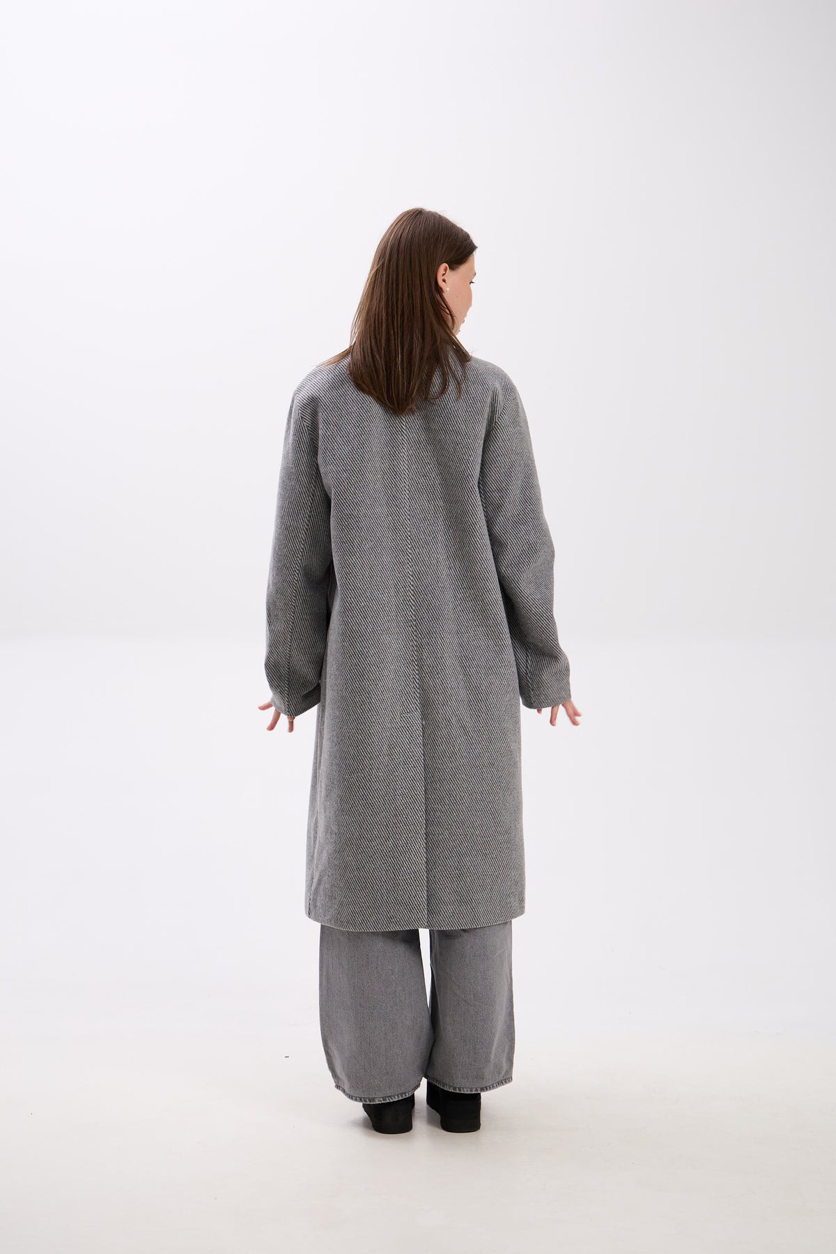 Person wearing a gray coat and pants on a white background