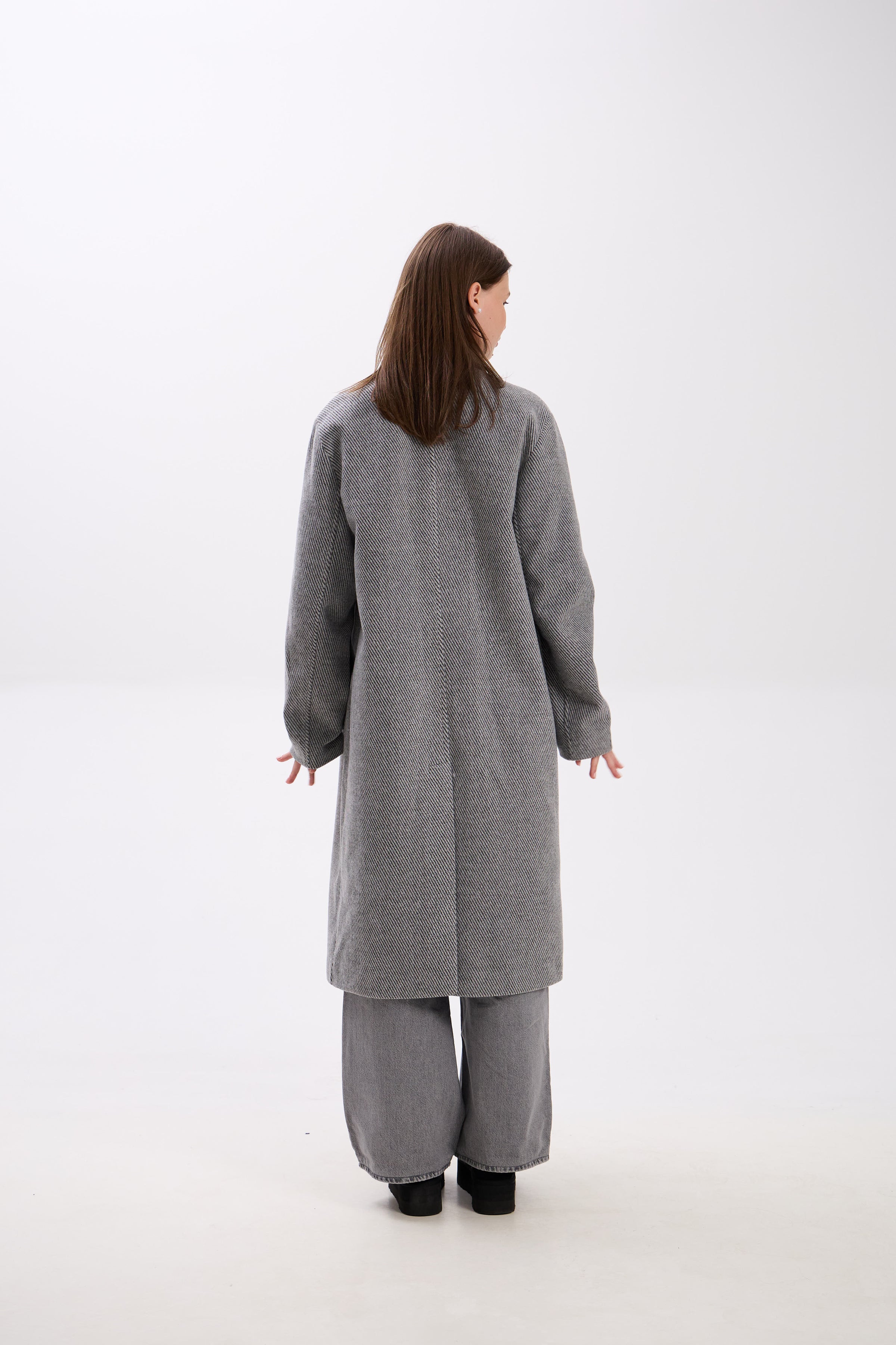 Person wearing a gray coat and pants on a white background