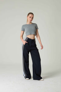 Woman wearing a gray crop top and black pants with white stripes on a light gray background.