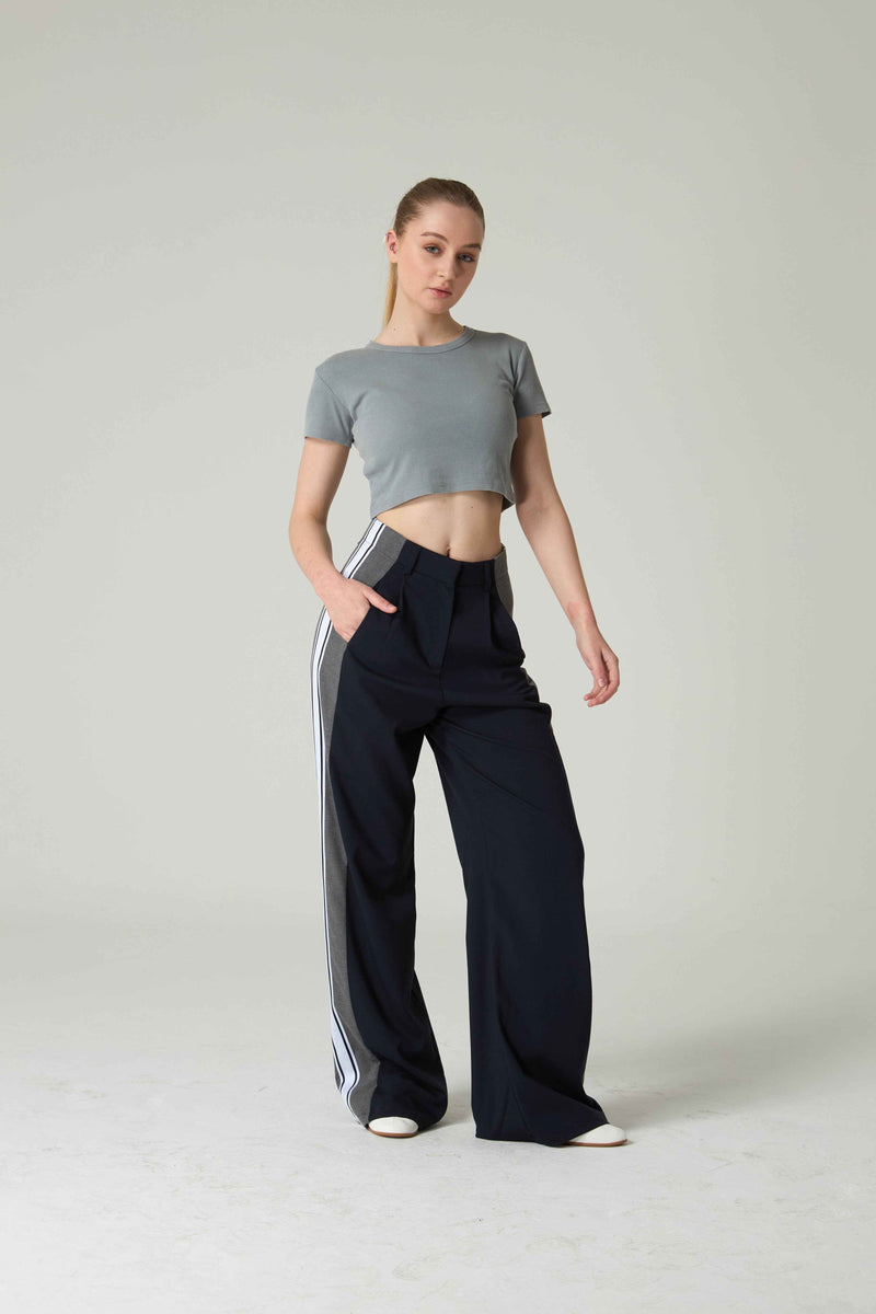 Woman wearing a gray crop top and black pants with white stripes on a light gray background.