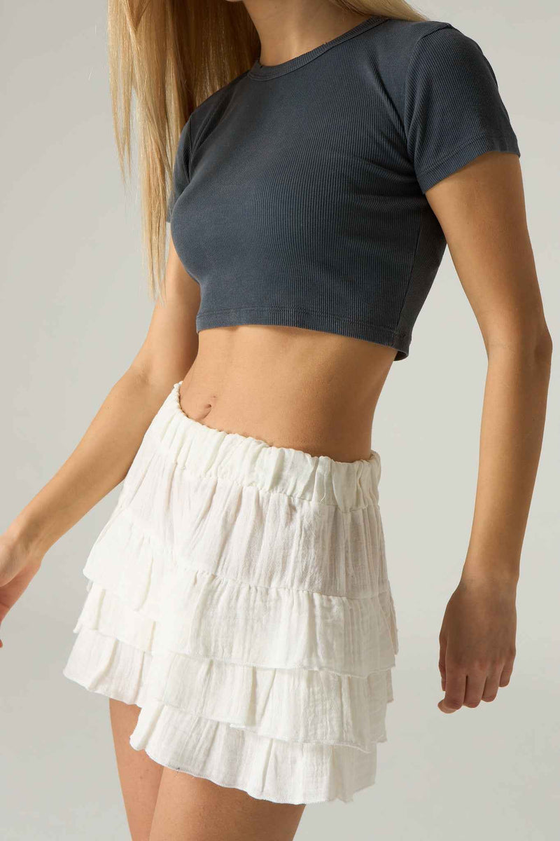 Person wearing a dark gray crop top and white tiered skirt on a plain background.