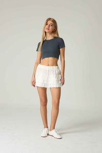 Woman wearing a dark gray crop top and white shorts on a plain background.