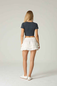 Person wearing a dark blue crop top and white pleated skirt on a plain background.