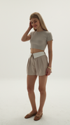 Woman wearing a beige crop top and shorts on a white background.