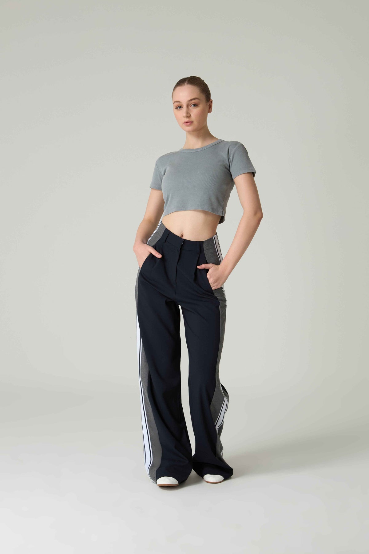 Woman wearing a gray crop top and black pants with white stripes on a plain background.