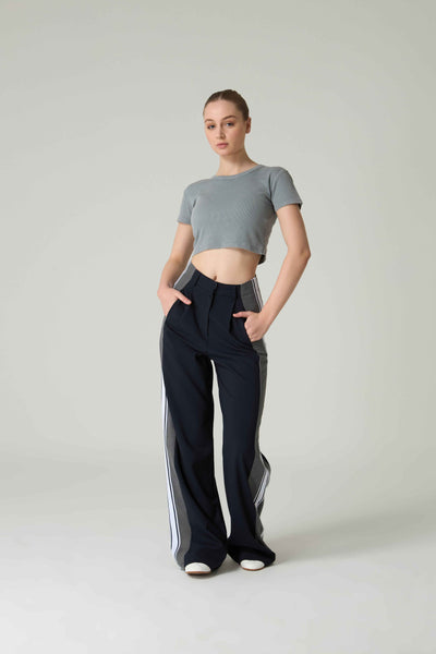 Woman wearing a gray crop top and black pants with white stripes on a plain background.