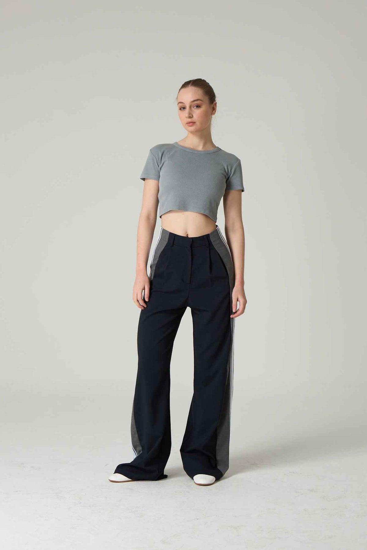 Woman wearing a gray crop top and navy wide-leg pants on a plain background.