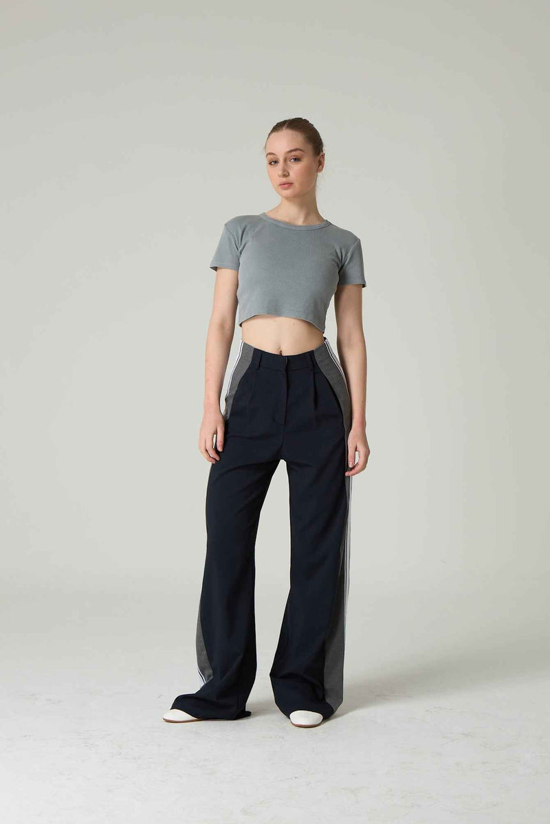 Woman wearing a gray crop top and navy wide-leg pants on a plain background.