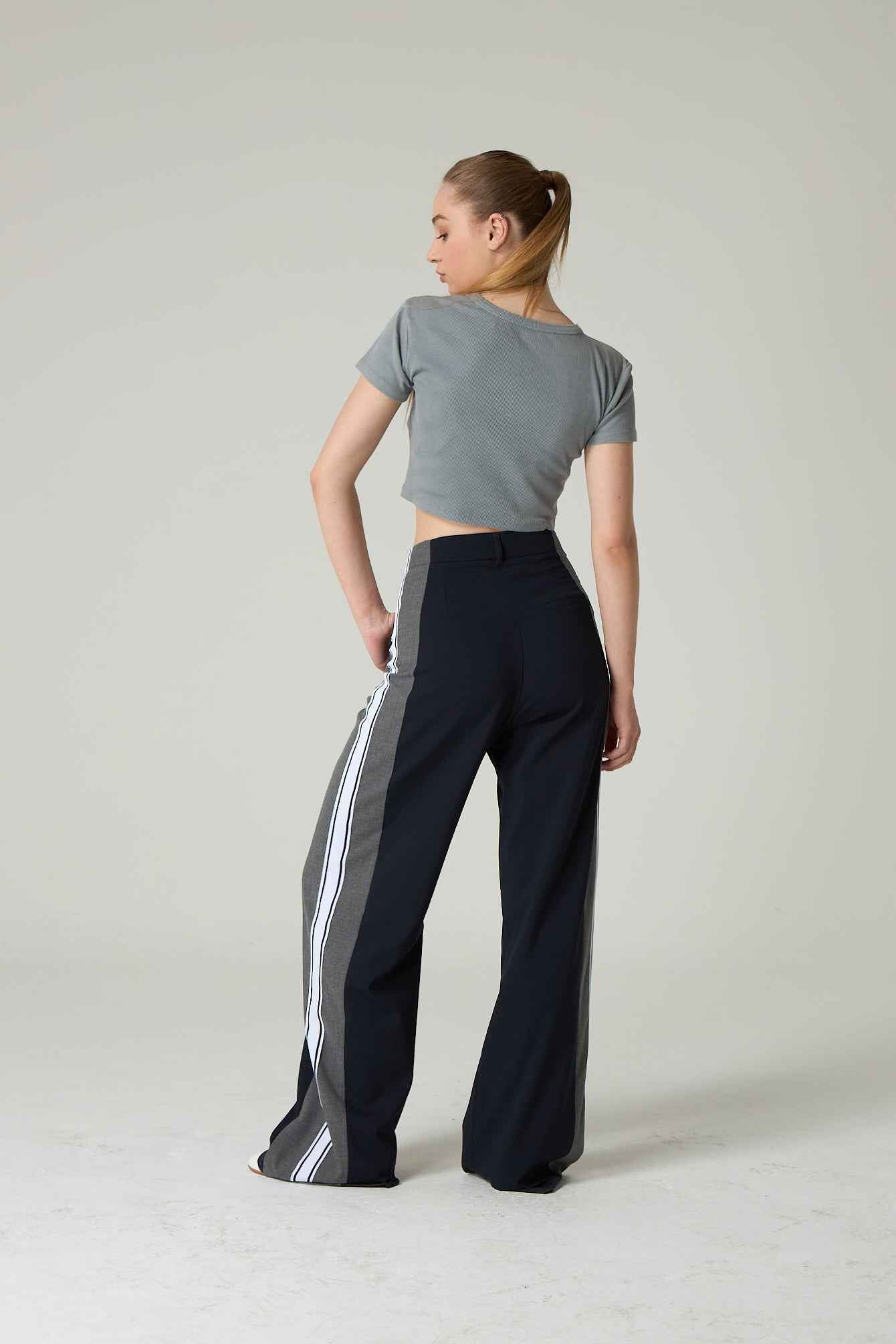 Woman wearing a gray crop top and black pants with white stripes on a plain background.