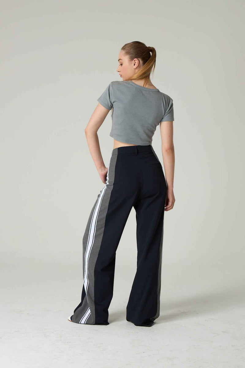 Woman wearing a gray crop top and black pants with white stripes on a plain background.