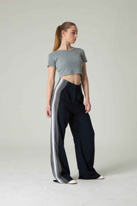 Woman wearing a gray crop top and black pants with white stripes on a plain background.