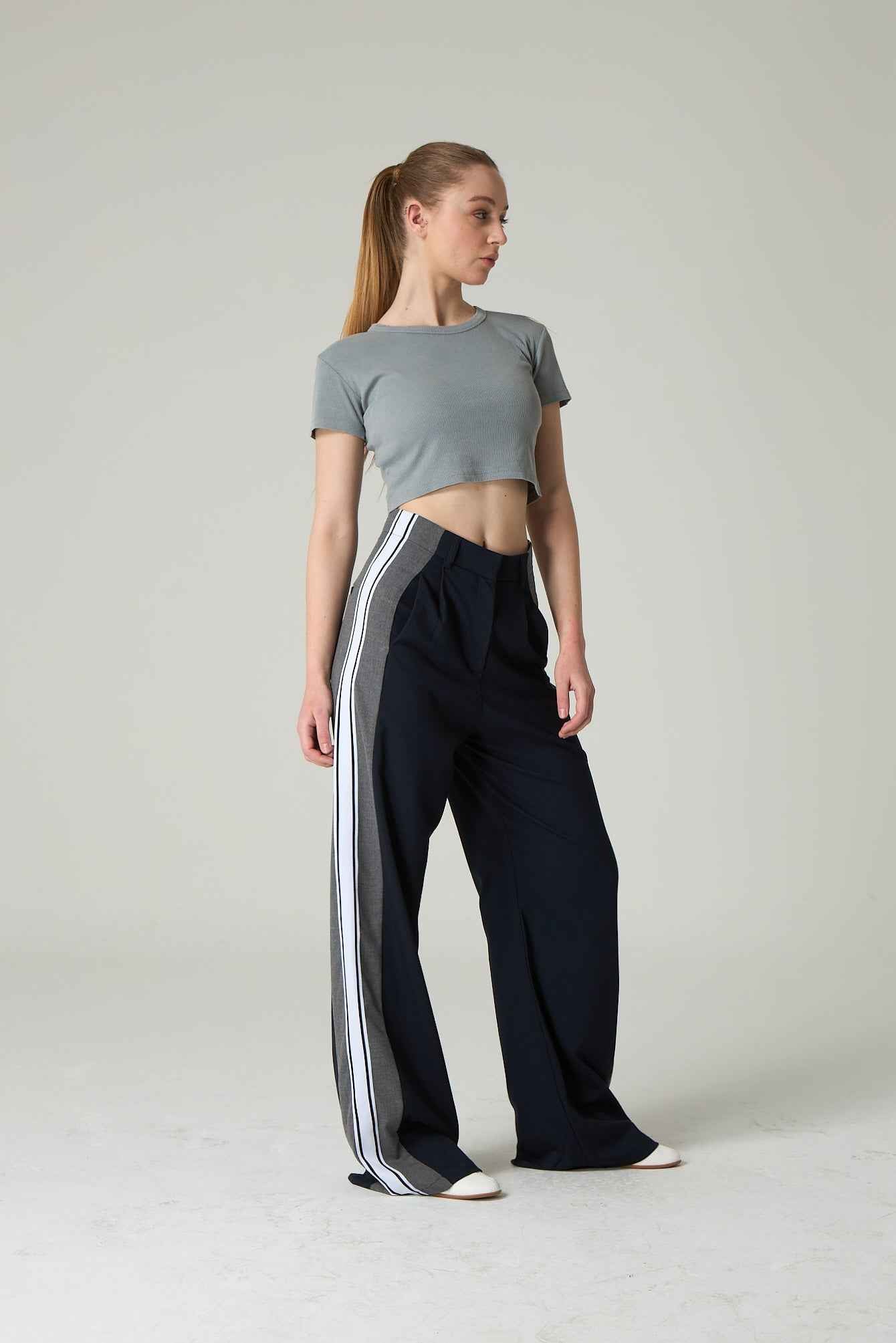 Woman wearing a gray crop top and black pants with white stripes on a plain background.