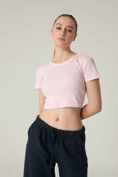 Person wearing a pink crop top and black pants on a plain background.