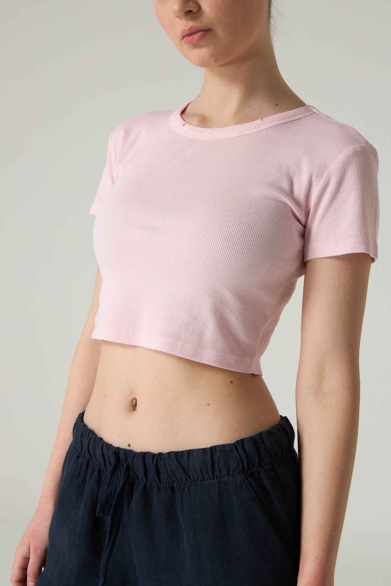 Person wearing a pink crop top and dark pants against a plain background.