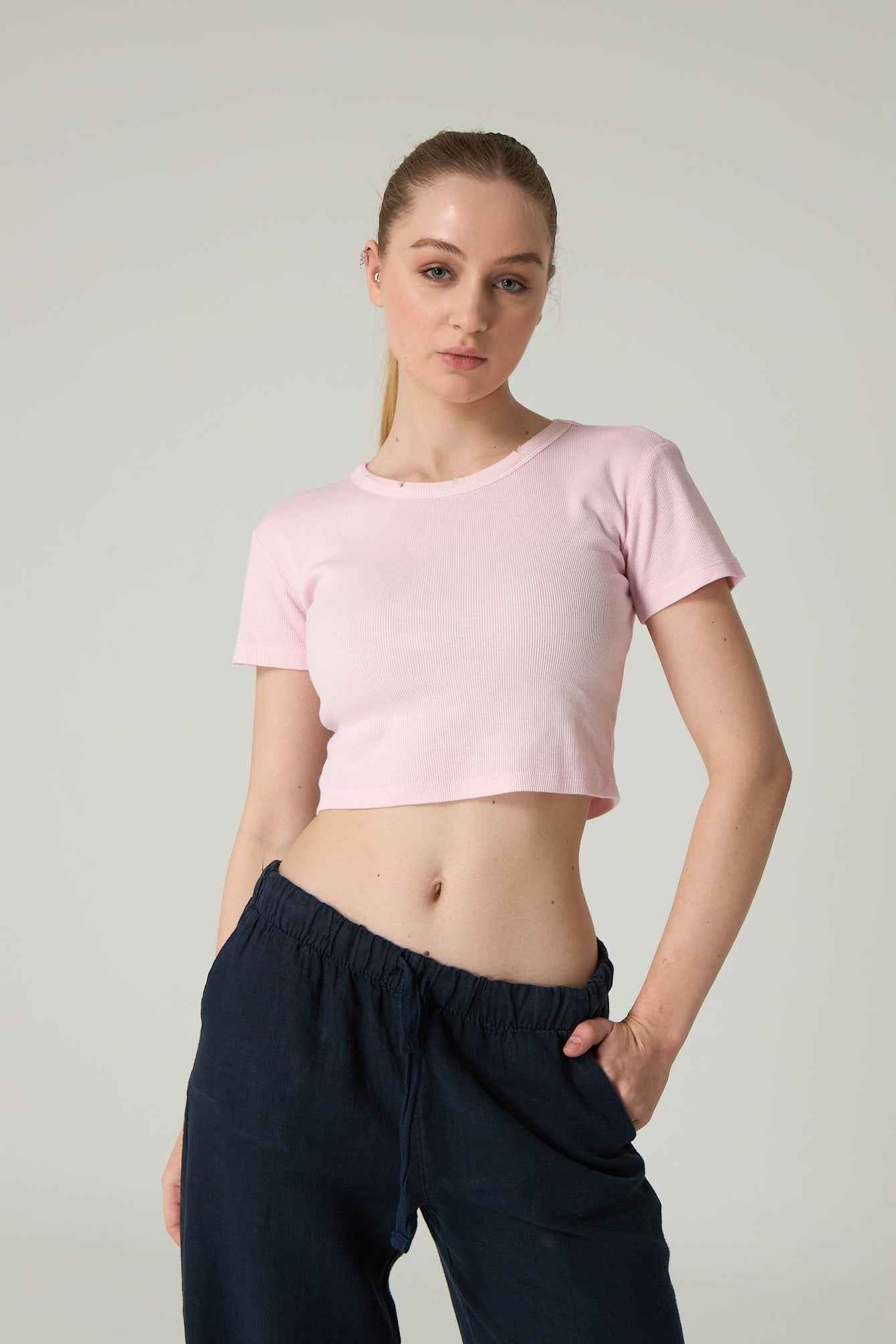 Woman wearing a pink crop top and navy pants against a plain background.
