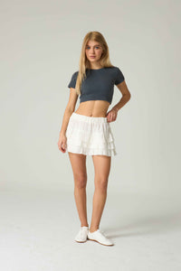 Woman wearing a dark blue crop top and white skirt on a plain background.