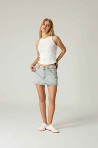 Woman wearing a white sleeveless top and light blue denim skirt on a plain background.