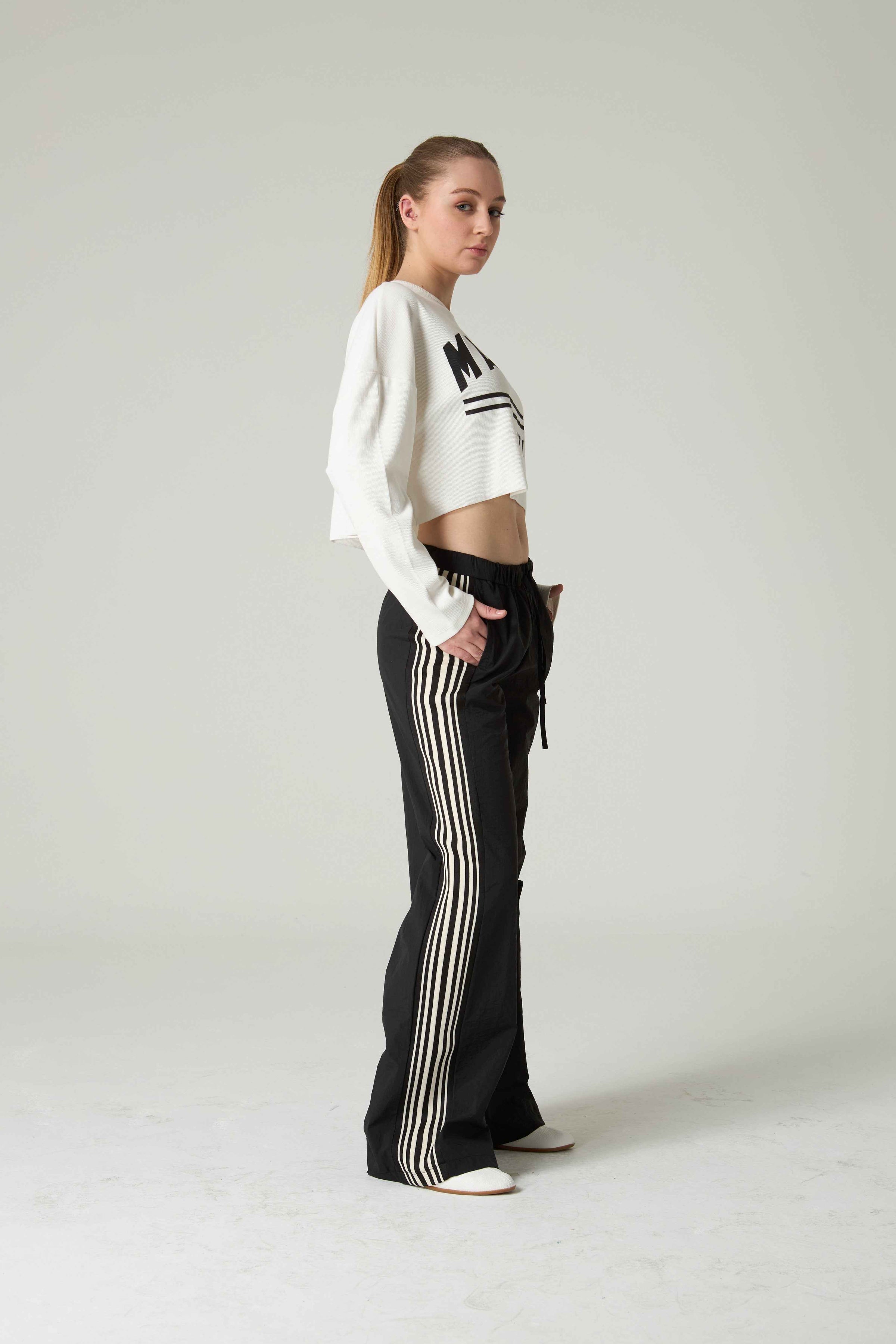 Woman wearing a white cropped sweater and black pants with white stripes on a plain background.