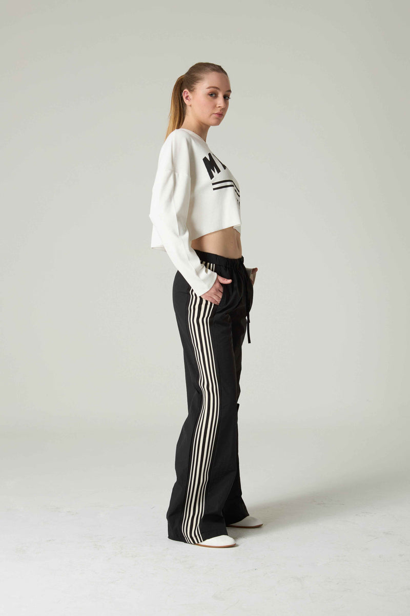 Woman wearing a white cropped sweater and black pants with white stripes on a plain background.
