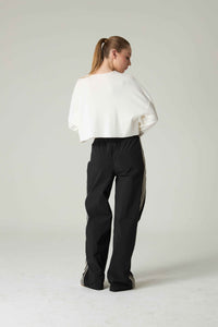 Person wearing a white top and black pants with stripes on a light gray background.