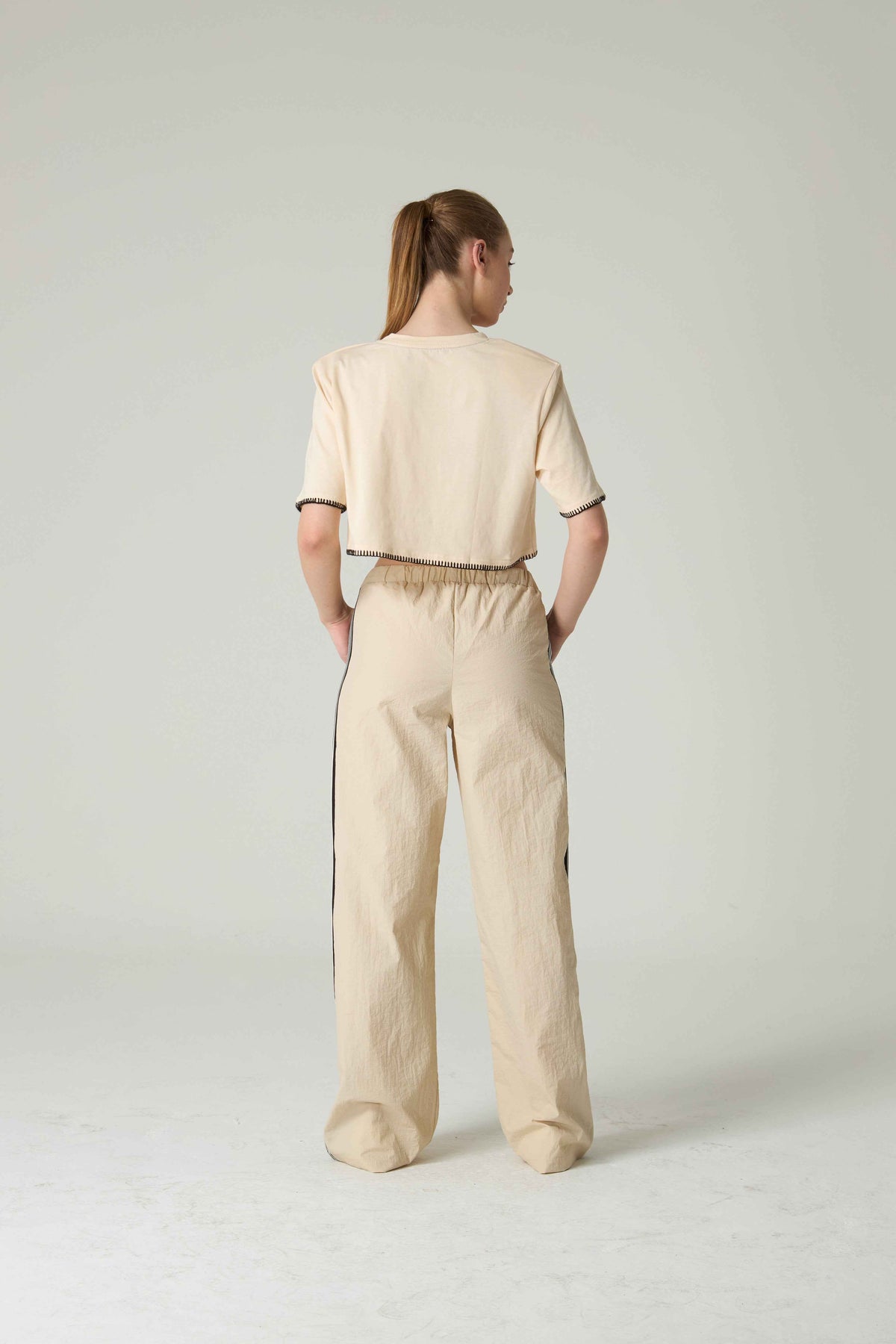 Person wearing a beige outfit with black trim on a white background.