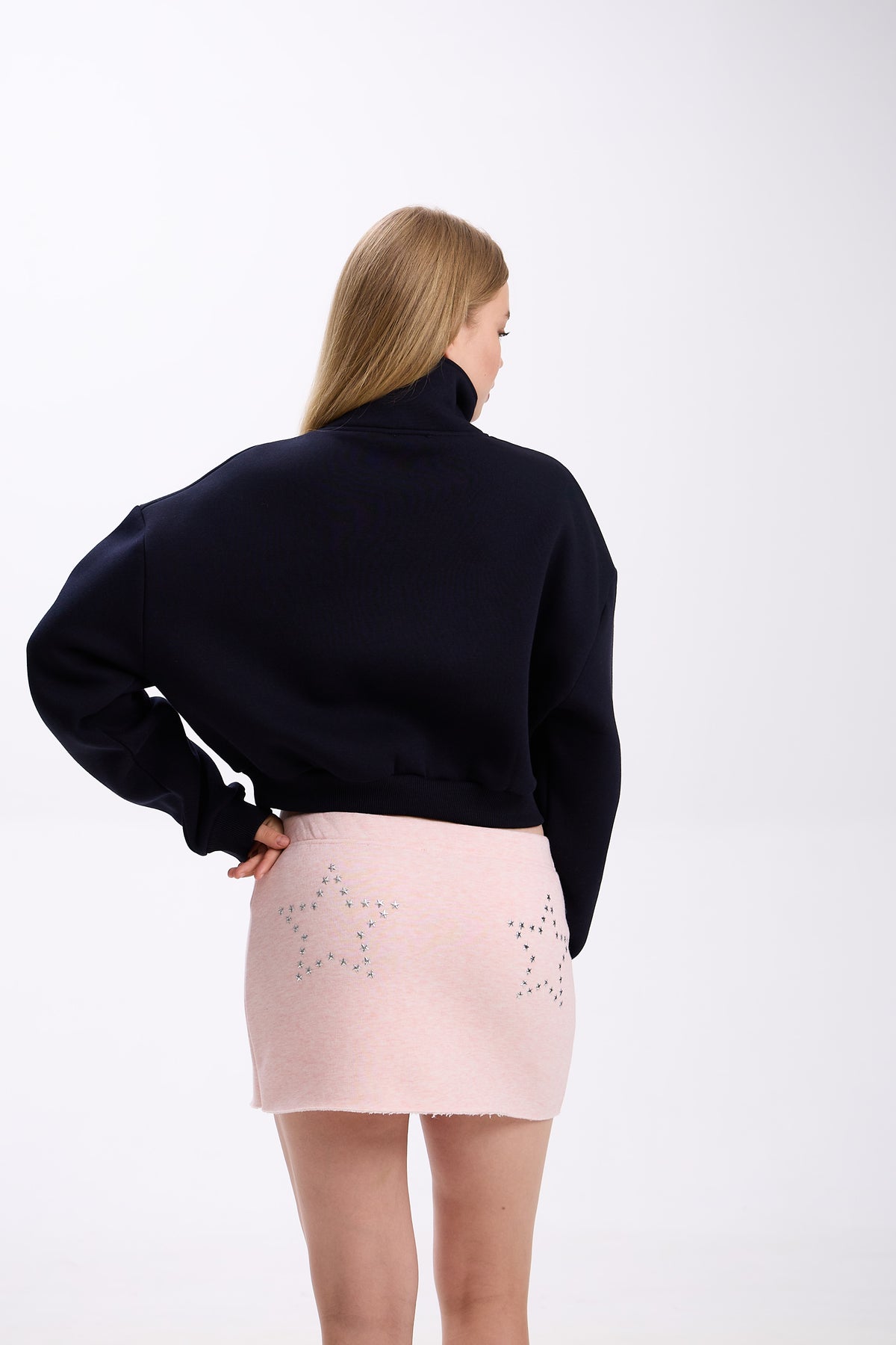 Person wearing a black sweater and pink skirt on a white background.