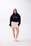 Navy cropped half-zip hoodie with ‘STAY CLOSE’ embroidery, styled with pastel pink mini skirt and white sneakers – minimal streetwear look on plain backdrop (appears dark, similar to black).