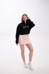 Navy cropped half-zip hoodie with bold white 'STAY CLOSE' embroidery, styled with pastel pink mini skirt and casual white sneakers – full-body streetwear look, hair-touch pose on plain backdrop (dark navy shade close to black)